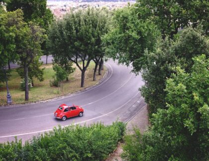 Una cinquecento rossa che passa su un viale alberato cittadino