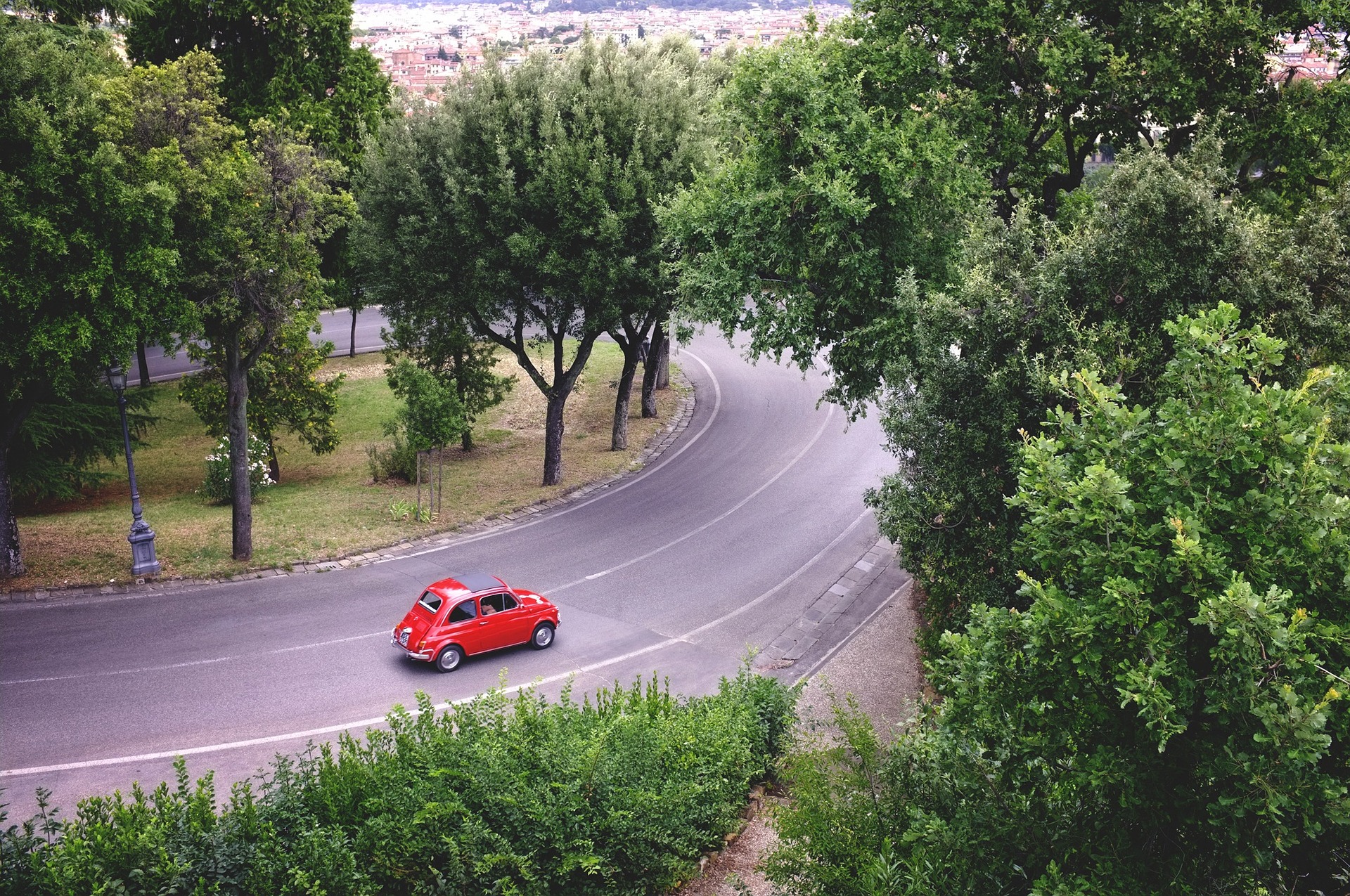 Una cinquecento rossa che passa su un viale alberato cittadino